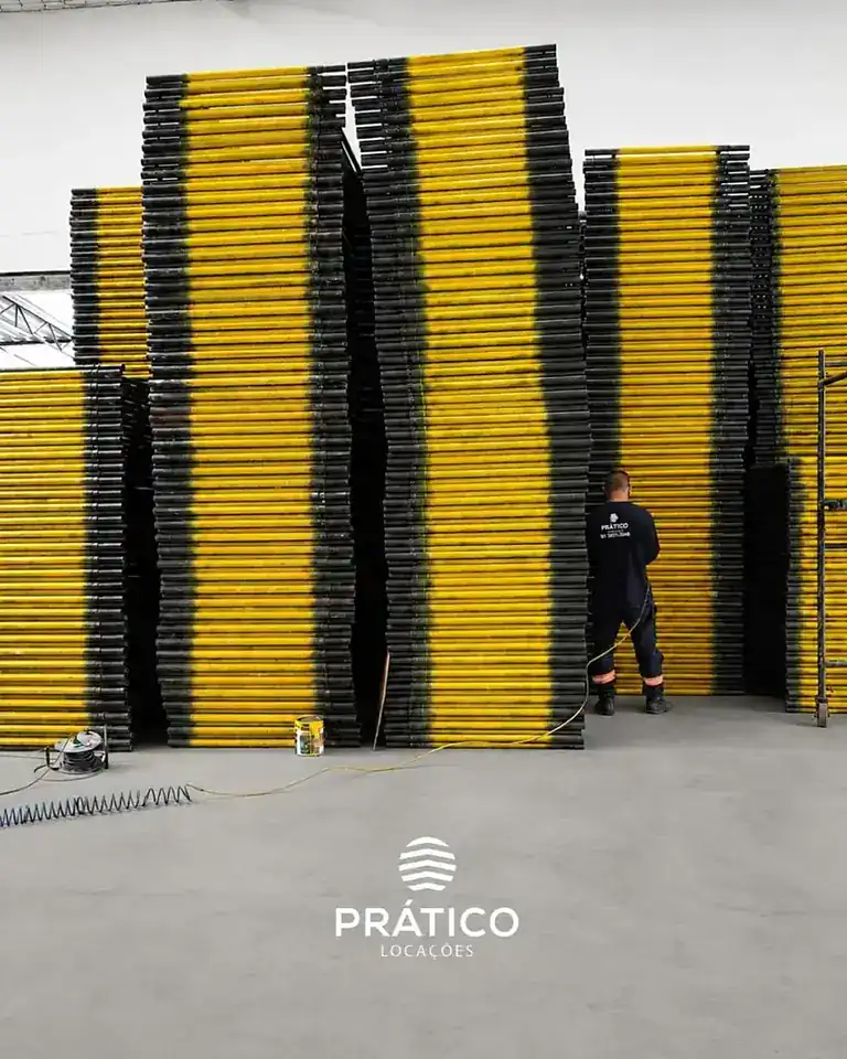 Pilhas de quadros de andaime tubular amarelo e preto no galpão da Prático Locações em Recife