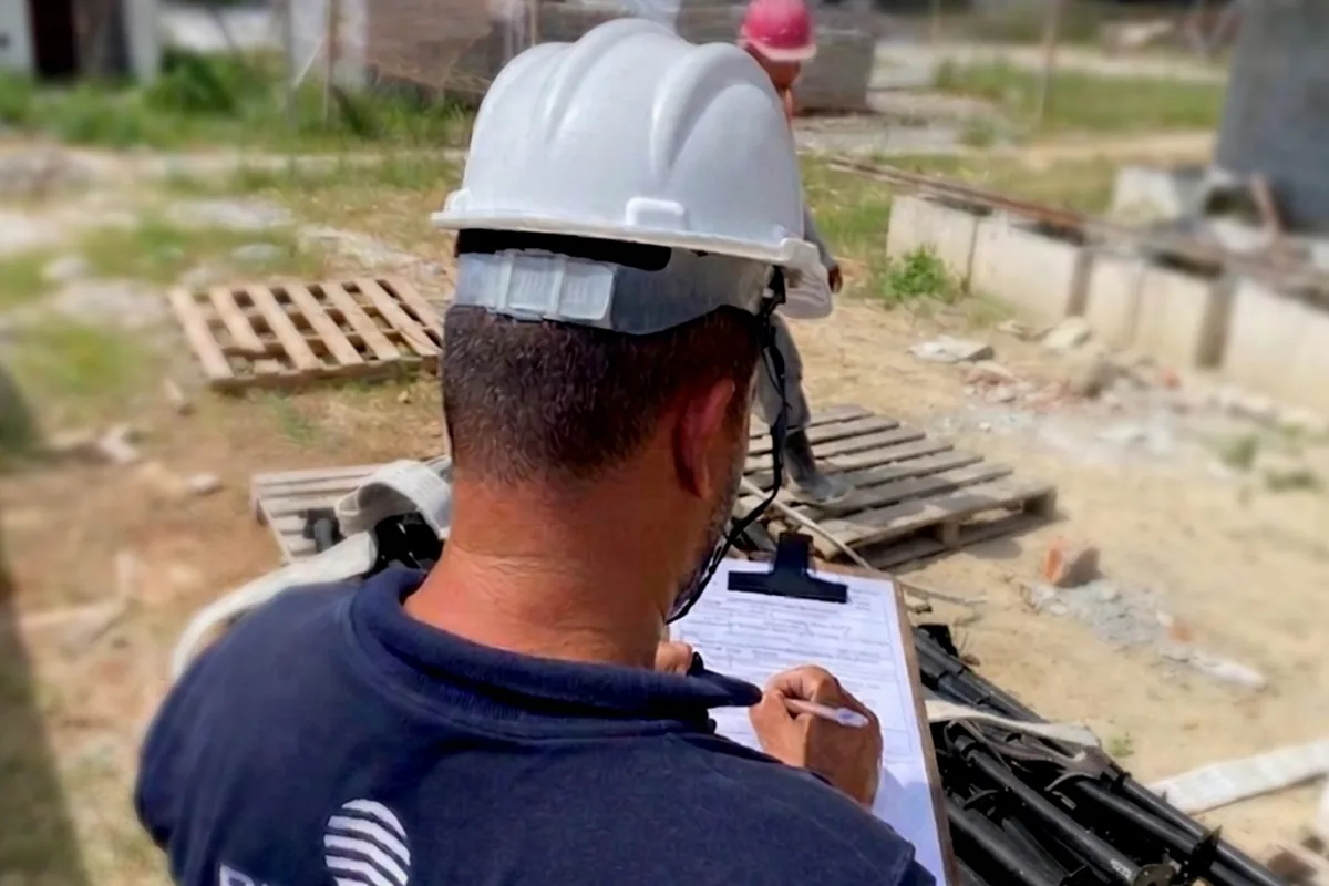 Técnico da Prático Locações de capacete conferindo na prancheta o equipamento entregue na obra